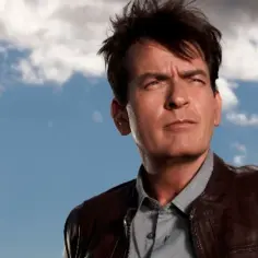 Charlie Sheen w skórzanej kurtce, zamyślony pod błękitnym niebem. Jego filmy, seriale i programy to niezapomniane historie.