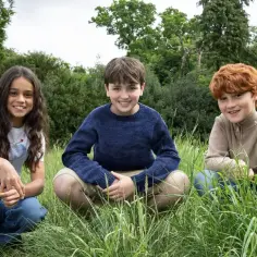 Trójka dzieci w trawie, jakby przygotowywała się do przygody w stylu Harry Potter 2025.