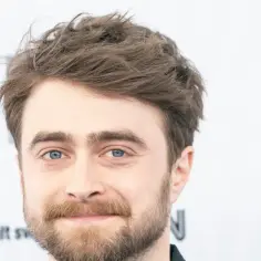 Daniel Radcliffe, znany z roli Harry'ego Pottera, z niebieskimi oczami i zarostem. W tle logo "MEN" i "adult swim".