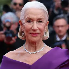 Helen Mirren w fioletowej sukni i biżuterii, otoczona przez fotoreporterów. Jej bogata kariera obejmuje liczne filmy, seriale i programy.