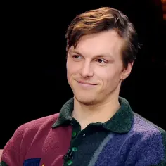 Tomasz Włosok w kolorowym swetrze, uśmiecha się, jakby opowiadał o swoich najnowszych filmach.