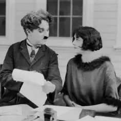 Charlie Chaplin z papierami rozmawia z kobietą. Może to scena z filmu, gdzie grał z dziećmi.