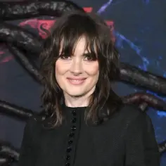 Winona Ryder, gwiazda filmów, seriali i programów, uśmiecha się na tle mrocznych, wijących się kształtów i logo Netflix.