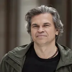 Jarosław Boberek, znany z ról w filmach, serialach i programach, w zielonej kurtce i z naszyjnikiem.