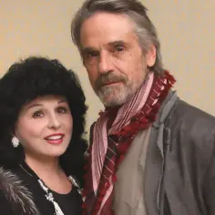 Jeremy Irons, znany z wielu filmów, pozuje z kobietą o bujnych, czarnych włosach i w futrzanym szalu.
