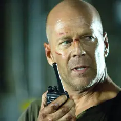 Bruce Willis w 2025 roku, z ranami na twarzy, trzyma krótkofalówkę.