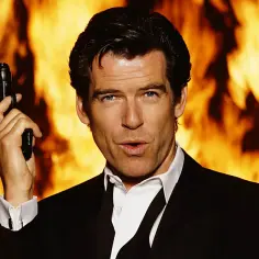 Pierce Brosnan w garniturze, z pistoletem w dłoni, na tle płomieni. Ikona kina akcji, znany z wielu filmów.