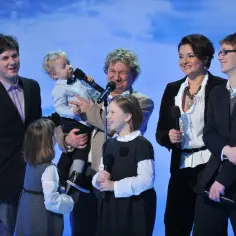 Paweł Królikowski z dziećmi na scenie. Wszyscy trzymają mikrofony, gotowi do występu.