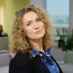 Portret Kamili Dreckiej, autorki artykułów na Wikipedii, z kręconymi blond włosami i okularami na głowie.