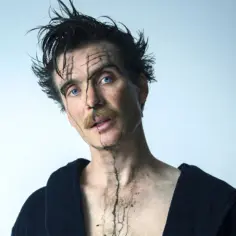 Cillian Murphy w filmach, z niebieskimi oczami i artystycznym makijażem na twarzy, w czarnym szlafroku.