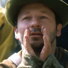 Zbigniew Zamachowski w historycznych filmach, z dłońmi przy twarzy, w zielonym kapeluszu.