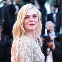 Elle Fanning, gwiazda filmów i seriali, na czerwonym dywanie otoczona przez fotoreporterów.