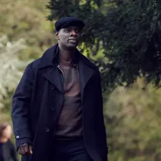 Omar Sy w eleganckim płaszczu i kaszkiecie, jakby prosto z jego filmów i seriali.