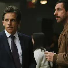 Dwóch znanych aktorów komediowych Hollywood, Ben Stiller w garniturze i Adam Sandler w brązowej kurtce, rozmawiają podczas wydarzenia.