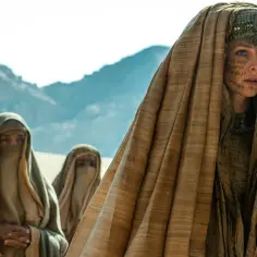 Kobiety w tradycyjnych strojach, w tym jedna z charakterystycznymi tatuażami na twarzy, należące do zakonu **Bene Gesserit**, przemierzają pustynię.