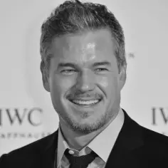 Uśmiechnięty Eric Dane, znany z filmów, seriali i programów, na tle logo IWC Schaffhausen.