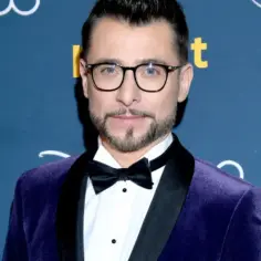 Kacper Kuszewski w fioletowym aksamitnym garniturze i czarnej muszce. Wygląda elegancko, jakby wybierał się na galę z żoną.