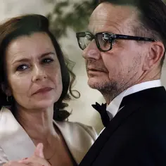 Para z eleganckimi strojami, kobieta patrzy w bok, mężczyzna w okularach w garniturze.