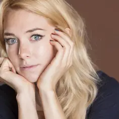 Portret Vanessy Kirby, aktorki znanej z wielu filmów, z dłońmi opartymi o twarz i błękitnymi oczami.