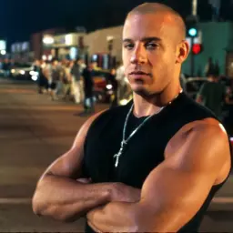 Vin Diesel w czarnej koszulce z krzyżem na szyi, gotowy do akcji w jednym z jego kultowych filmów.