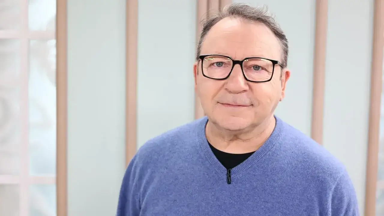 Zbigniew Zamachowski w niebieskim swetrze i okularach, gotowy do kolejnych ról w filmach.