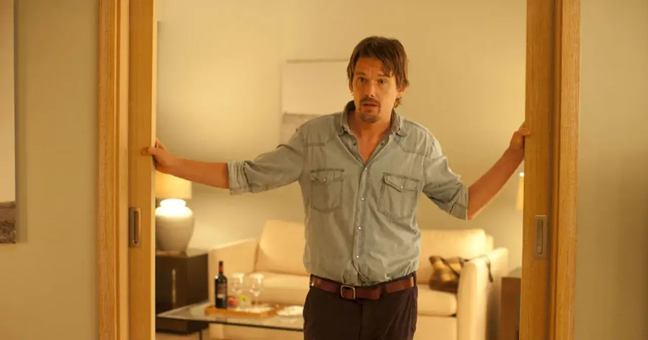 Ethan Hawke w dżinsowej koszuli otwiera drzwi, jakby zapraszał do świata jego filmów.