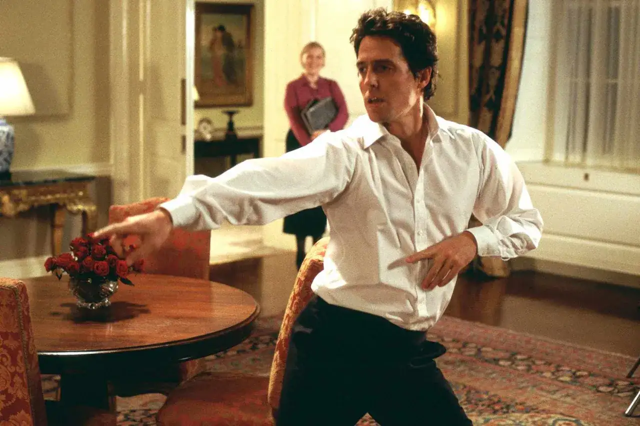Hugh Grant w białej koszuli tańczy w jednej ze swoich kultowych scen z filmów.