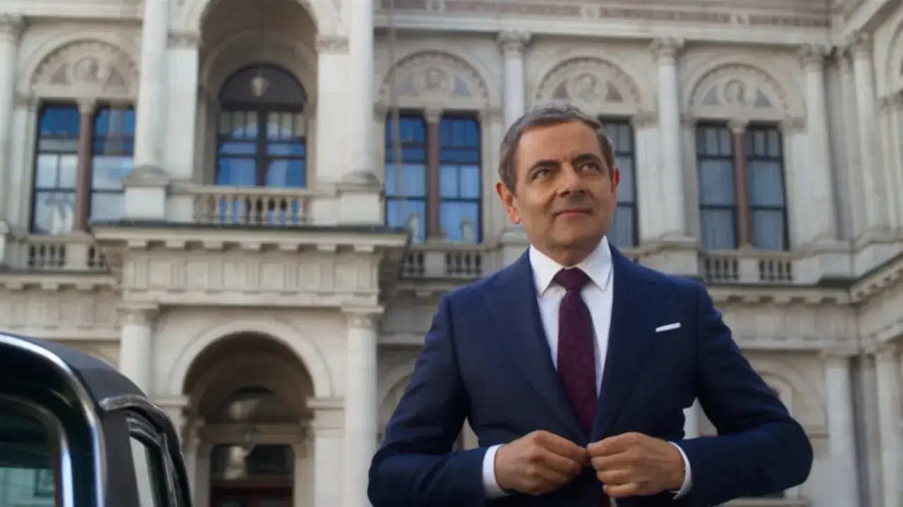 Elegancki Rowan Atkinson, czy żyje? Aktor w garniturze przed budynkiem.