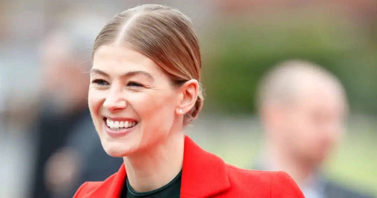 Uśmiechnięta Rosamund Pike, gwiazda filmów i seriali, w czerwonej marynarce.
