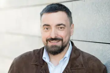 Mężczyzna z brodą i krótko ostrzyżonymi włosami, w brązowej kurtce, uśmiecha się. Może to bohater filmu braci Sekielskich?