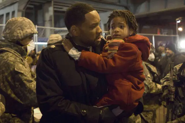 Robert Neville (Will Smith) trzyma córkę w ramionach, otoczony żołnierzami. Czy uda mu się przetrwać w świecie, gdzie jestem legendą 2?